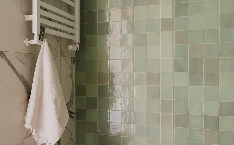 Współczesna łazienka z zielonymi kafelkami, białym grzejnikiem i drewnianym stołkiem.