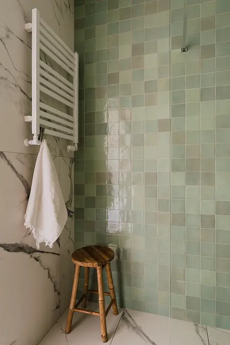 Współczesna łazienka z zielonymi kafelkami, białym grzejnikiem i drewnianym stołkiem.