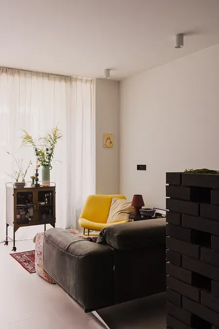 Współczesny salon z żółtym fotelem, szarym narożnikiem i roślinami.