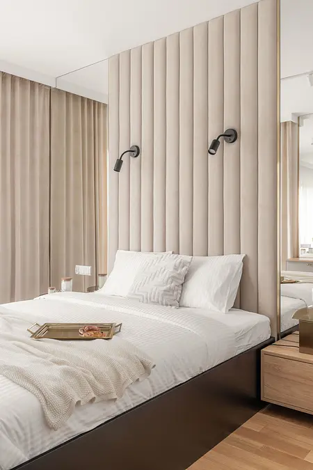 Wnętrze sypialni z beżową ścianą, białym łóżkiem i drewnianymi akcentami, styl współczesny.