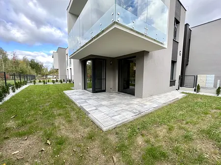 Widok nowoczesnego tarasu z szarymi płytkami i zielonym trawnikiem w stylu boho i współczesnym