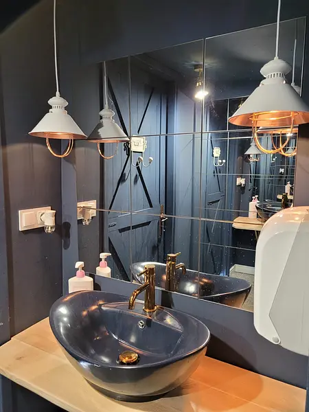 Nowoczesna łazienka z niebieskimi ścianami, złotą armaturą i eleganckimi lampami.