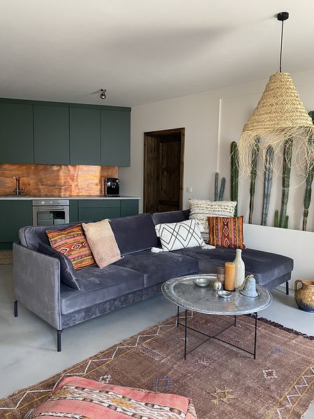 Wnętrze salonu boho z szarym narożnikiem i zieloną kuchnią