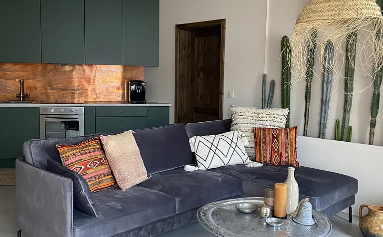 Wnętrze salonu boho z szarym narożnikiem i zieloną kuchnią