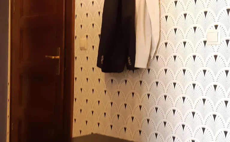 Przedpokój z czarną ławką, białą tapetą w stylu vintage i wieszakiem na ubrania.