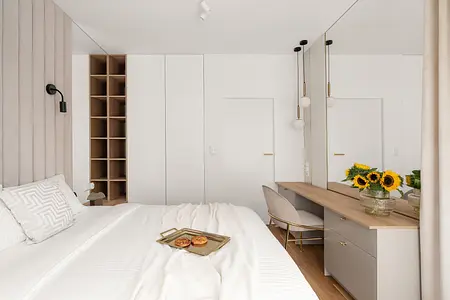 Współczesna sypialnia z białymi meblami, drewnianą półką i słonecznikami na biurku.