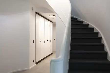 Przedpokój minimalistyczny z białymi szafkami i czarnymi schodami, styl minimaluxe, quiet luxury.
