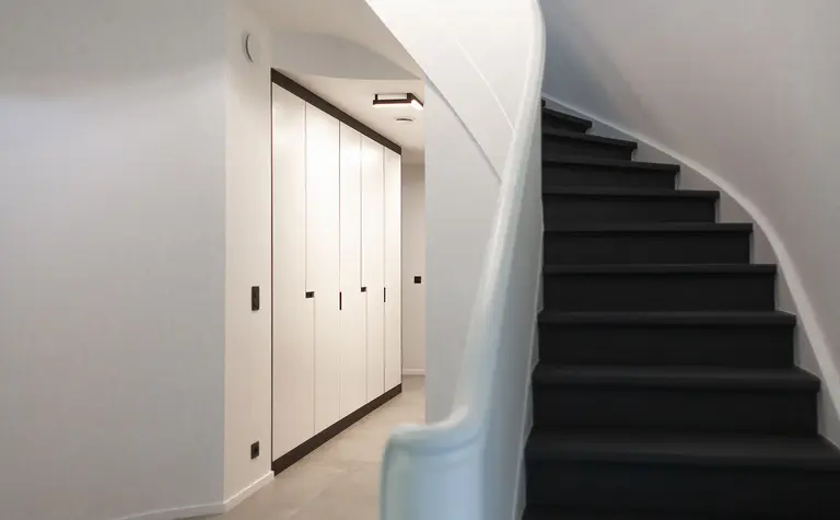 Przedpokój minimalistyczny z białymi szafkami i czarnymi schodami, styl minimaluxe, quiet luxury.