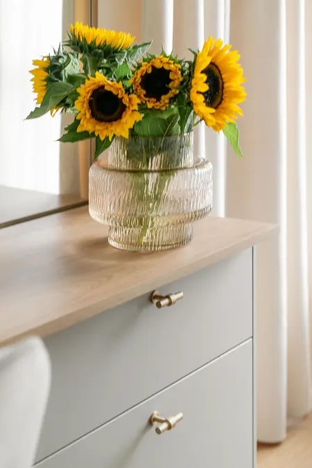 Wnętrze salonu z bukietem słoneczników w wazonie i jasnymi meblami.