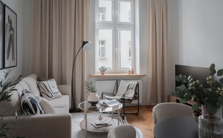 Nowoczesny salon w stylu skandynawskim z beżowymi zasłonami i minimalistycznymi meblami.