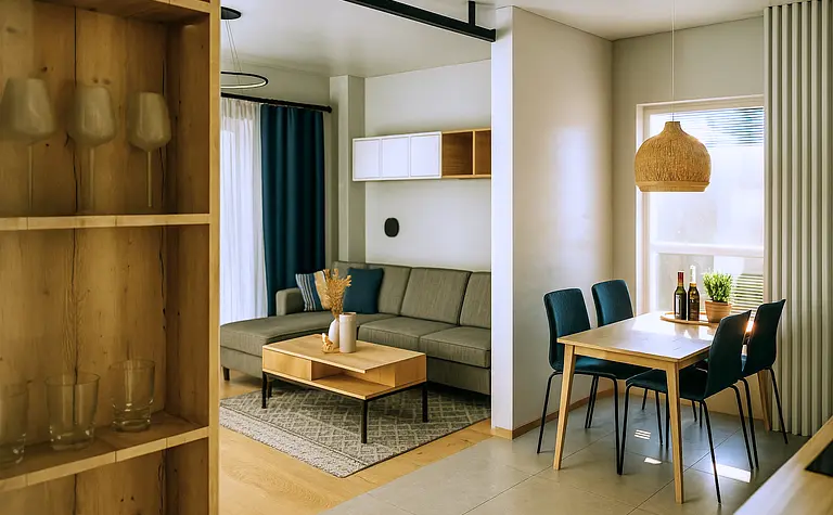 Wnętrze salonu w stylu skandynawskim z szarym narożnikiem, drewnianym stołem i roślinnością.