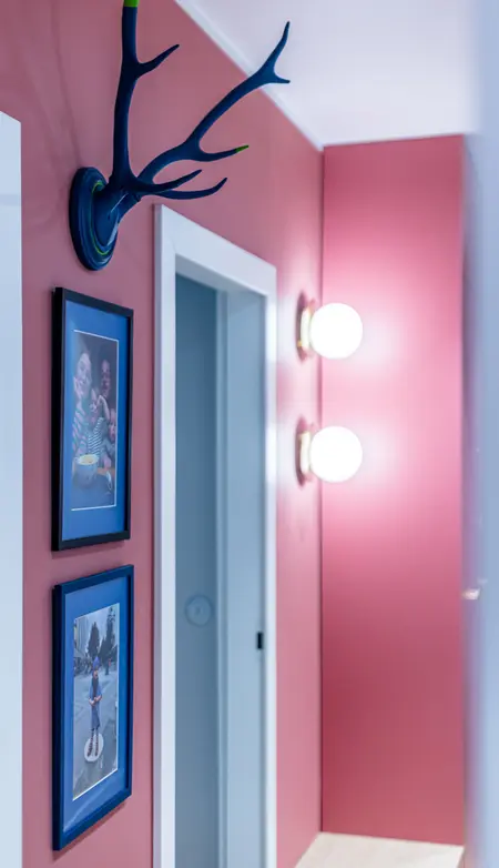 Przedpokój z różowymi ścianami, zdjęciami w ramkach oraz oświetleniem, styl dopamine decor, vintage.