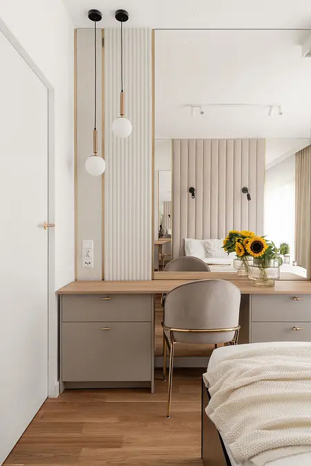 Stylowe wnętrze sypialni z drewnianym biurkiem, lustrem i kwiatami.