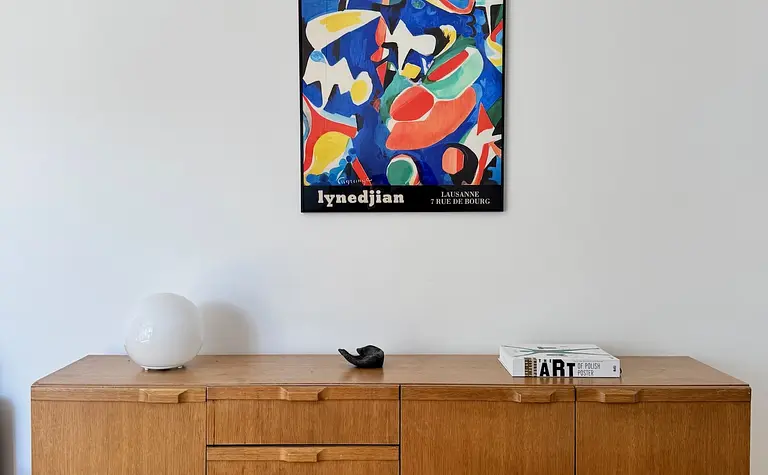 Eklektyczne wnętrze salonu z drewnianą komodą i nowoczesnym obrazem w stylu skandynawskim.