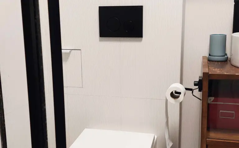 Wnętrze łazienki z białą toaletą, drewnianymi meblami i minimalistycznymi detalami.