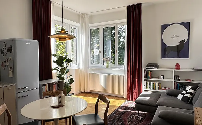 Wnętrze eklektycznego salonu z czerwonymi zasłonami i drewnianą podłogą.