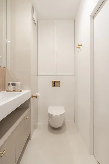 Wnętrze łazienki z białymi kafelkami, umywalką i złotymi akcentami. Styl współczesny.