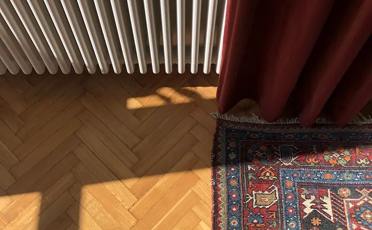 Wnętrze z eklektycznym dywanem, skandynawskim grzejnikiem i vintage zasłonami.