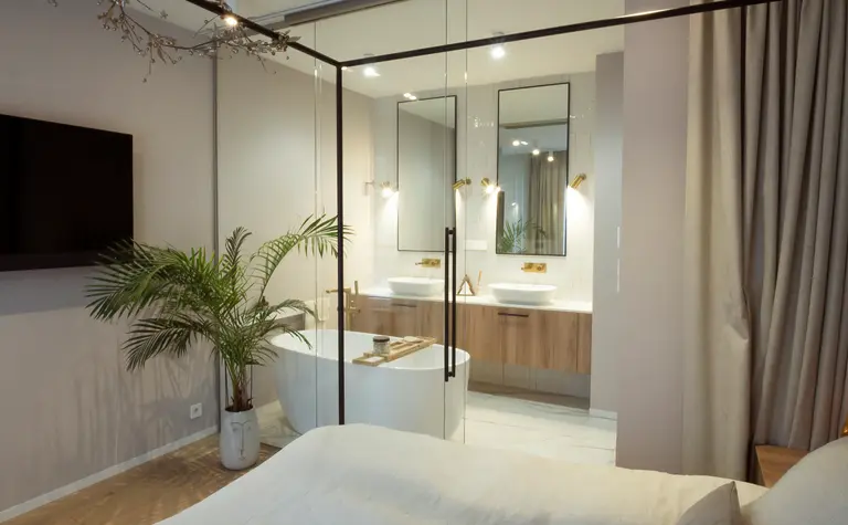 Sypialnia z łazienką, nowoczesne meble i rośliny w stylu quiet luxury.