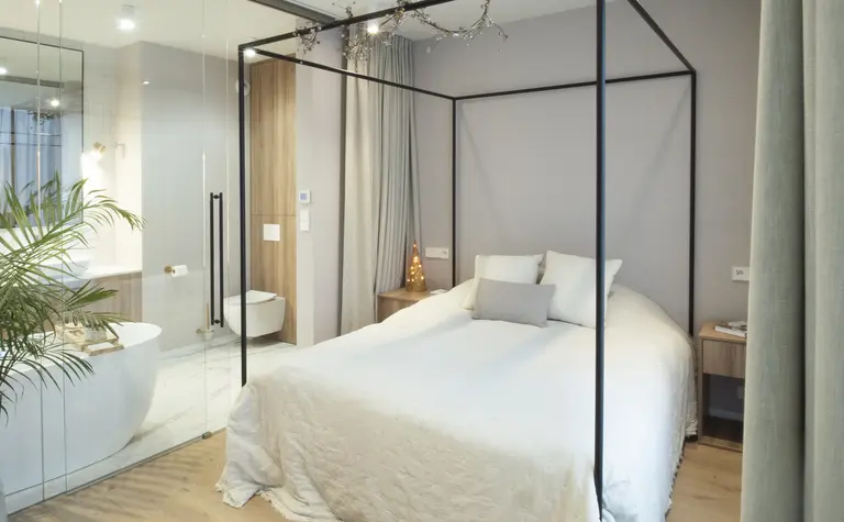 Sypialnia z łóżkiem, drewnianymi detalami i strefą łazienki w stylu quiet luxury.