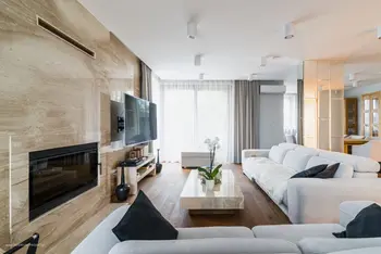 Nowoczesny salon z dużą, białą sofą, kamienną ścianą z wbudowanym kominkiem, telewizorem na ścianie, drewnianą podłogą oraz stolikiem kawowym.