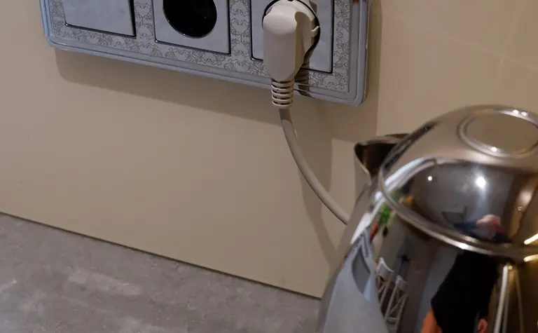 Gniazdko elektryczne na ścianie z metalowym czajnikiem w tradycyjnej kuchni.