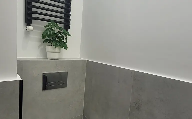 Minimalistyczna toaleta z szarymi płytkami i białą miską ustępową.