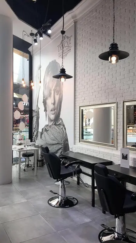 Salon fryzjerski z białymi ścianami, lustrami i stylowymi lampami w stylu glamour.