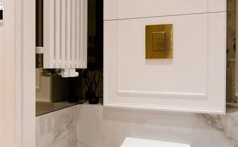 Nowoczesna łazienka z białą toaletą, złotymi detalami i marmurowymi ścianami, styl quiet luxury.