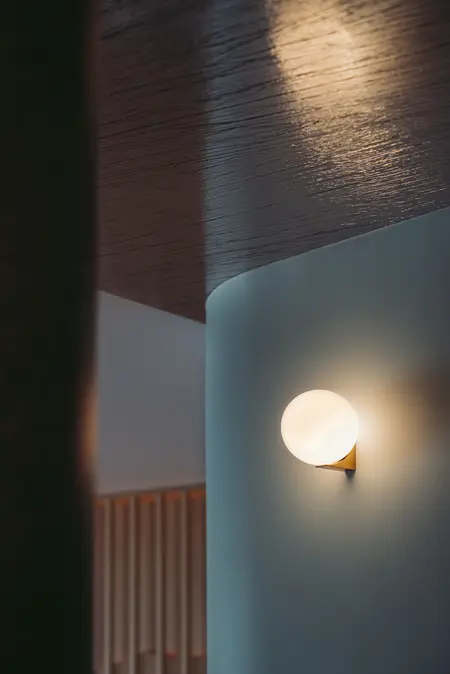 Eklektyczne wnętrze z nowoczesnym oświetleniem, drewnianymi detalami i minimalistycznym stylem.
