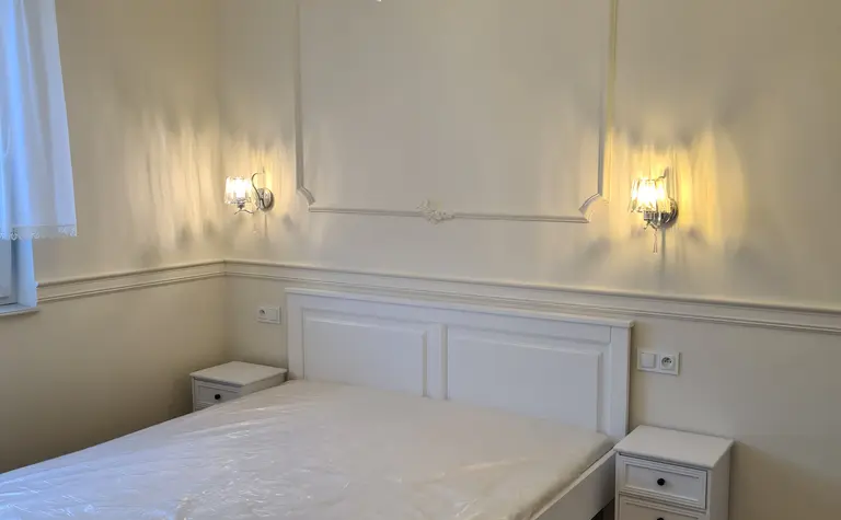 Tradycyjna sypialnia z białym łóżkiem, lustrami i eleganckim oświetleniem.