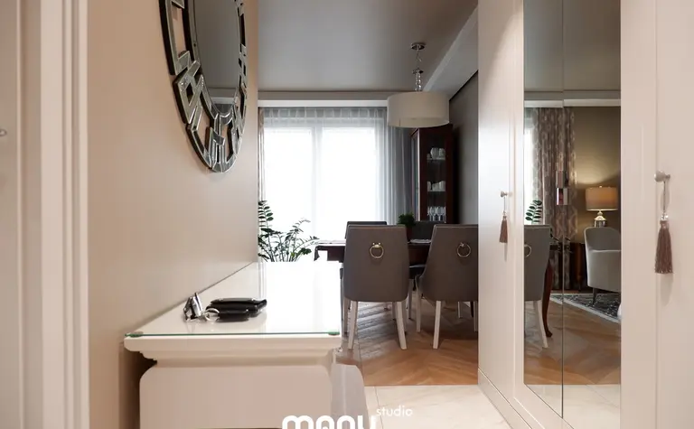 Przestronny przedpokój z lustrem, drewnianą podłogą, roślinami i eleganckimi meblami.