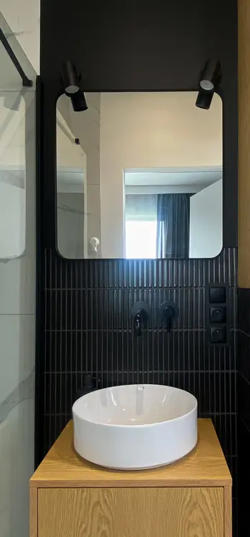 Minimalistyczna łazienka z białą umywalką i czarnymi akcentami w skandynawskim stylu.