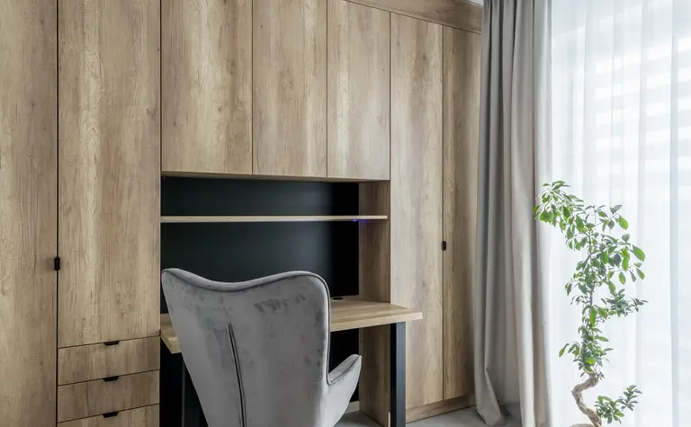 Wnętrze gabinetu z drewnianą zabudową, nowoczesnym biurkiem i rośliną. Styl minimalistyczny.