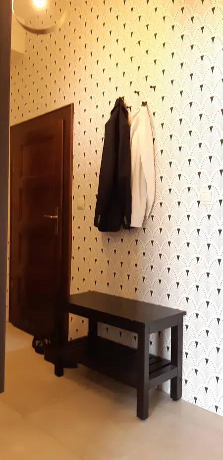 Przedpokój z czarną ławką, białą tapetą w stylu vintage i wieszakiem na ubrania.
