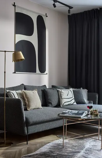 Wnętrze nowoczesnego salonu z szarym sofa, dekoracyjnymi poduszkami i stylowym oświetleniem.