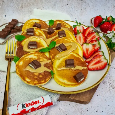 Pancakes z czekoladą Kinder, truskawkami i miętą na talerzu, styl art deco.
