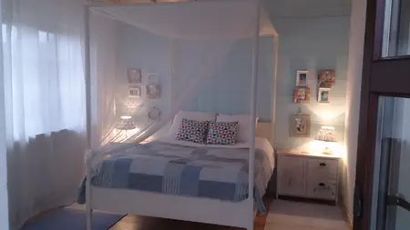 Sypialnia z białym łóżkiem, niebieską pościelą, boho i rustykalnymi dodatkami.