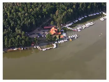 Widok portu z jachtami i drewnianym domkiem otoczonym zielenią. Minimalistyczny i nowoczesny styl.