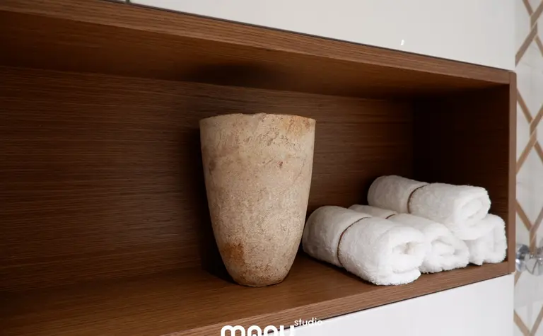 Wnętrze łazienki z drewnianymi półkami, ceramicznym wazonem i białymi ręcznikami.