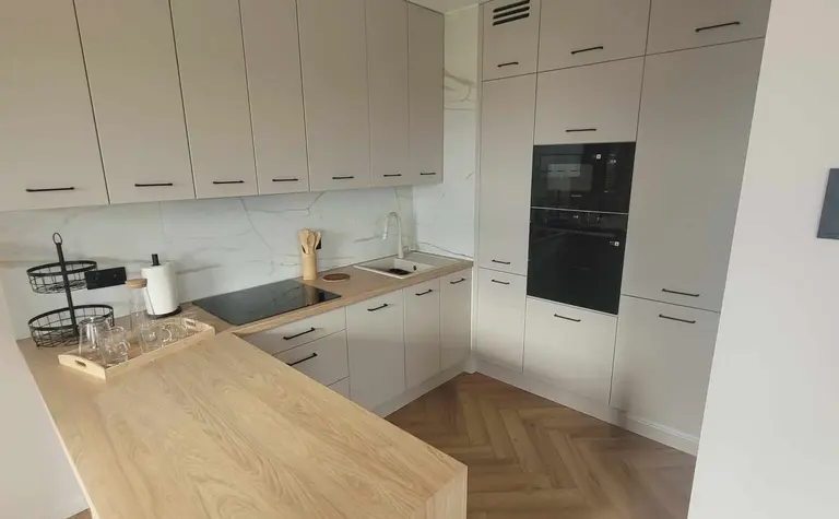Nowoczesna kuchnia z szarymi meblami i drewnianą wyspą, idealna do gotowania.