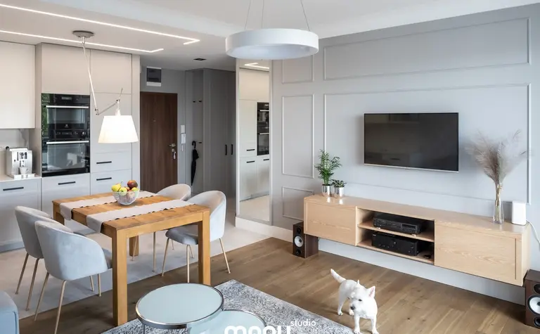 Nowoczesne wnętrze z drewnianym stołem, szarymi meblami, elementami art deco, quiet luxury i tradycyjnymi akcentami.