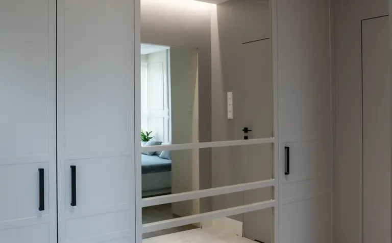 Garderoba z szarymi szafami, dużym lustrem i nowoczesnym oświetleniem. Styl art deco i tradycyjny.