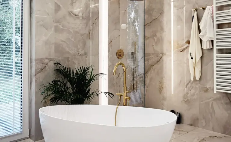 Nowoczesna łazienka glamour z białą wanną i złotymi detalami.