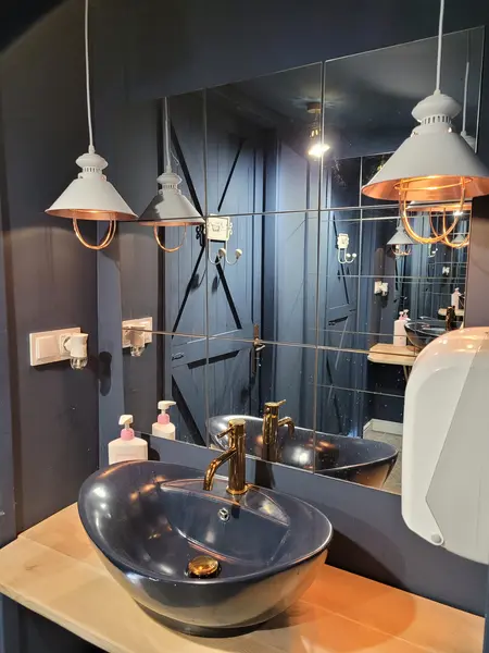 Nowoczesna łazienka z niebieskimi ścianami, złotą armaturą i eleganckimi lampami.