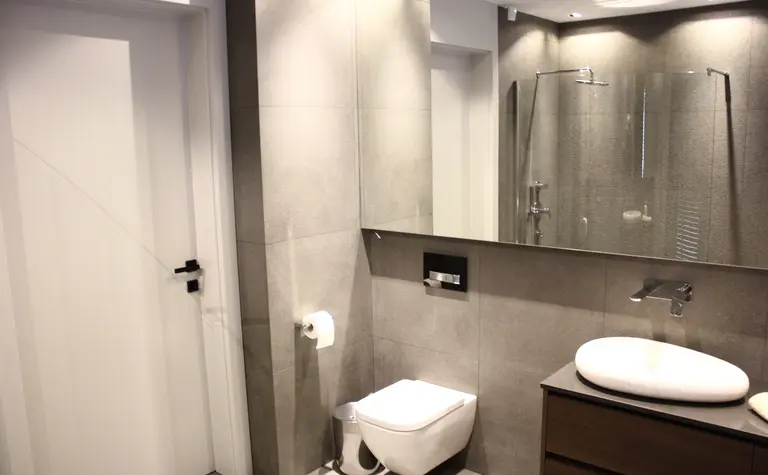 Nowoczesna łazienka z minimalistycznym designem, szarymi płytkami i białą umywalką.