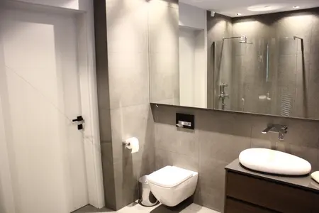 Nowoczesna łazienka z minimalistycznym designem, szarymi płytkami i białą umywalką.
