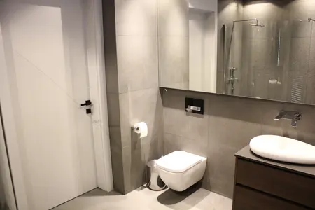 Nowoczesna łazienka z minimalistycznym wyposażeniem, szarymi płytkami i białą umywalką.