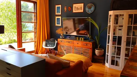 Wnętrze salonu z brązową sofą, żółtymi zasłonami i dekoracjami w stylu boho i eklektycznym.