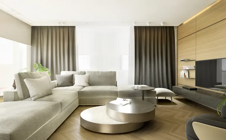 Przestronny salon z beżową narożną sofą, okrągłymi stolikami kawowymi, drewnianą podłogą w jodełkę, stylowymi zasłonami i minimalistycznymi półkami przy telewizorze